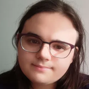 Picture of me. I smile slightly and have dark hair and red glasses and am lit from the side by the sun and also i have white skin.